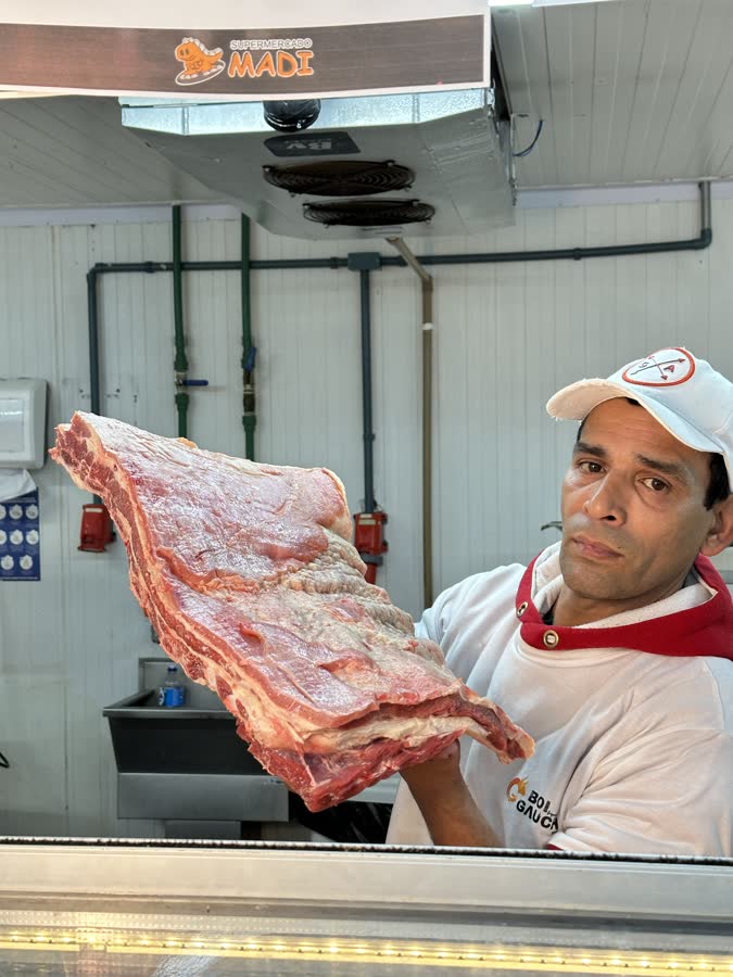 Açougueiro do Supermercado Madi segurando uma peça de costela