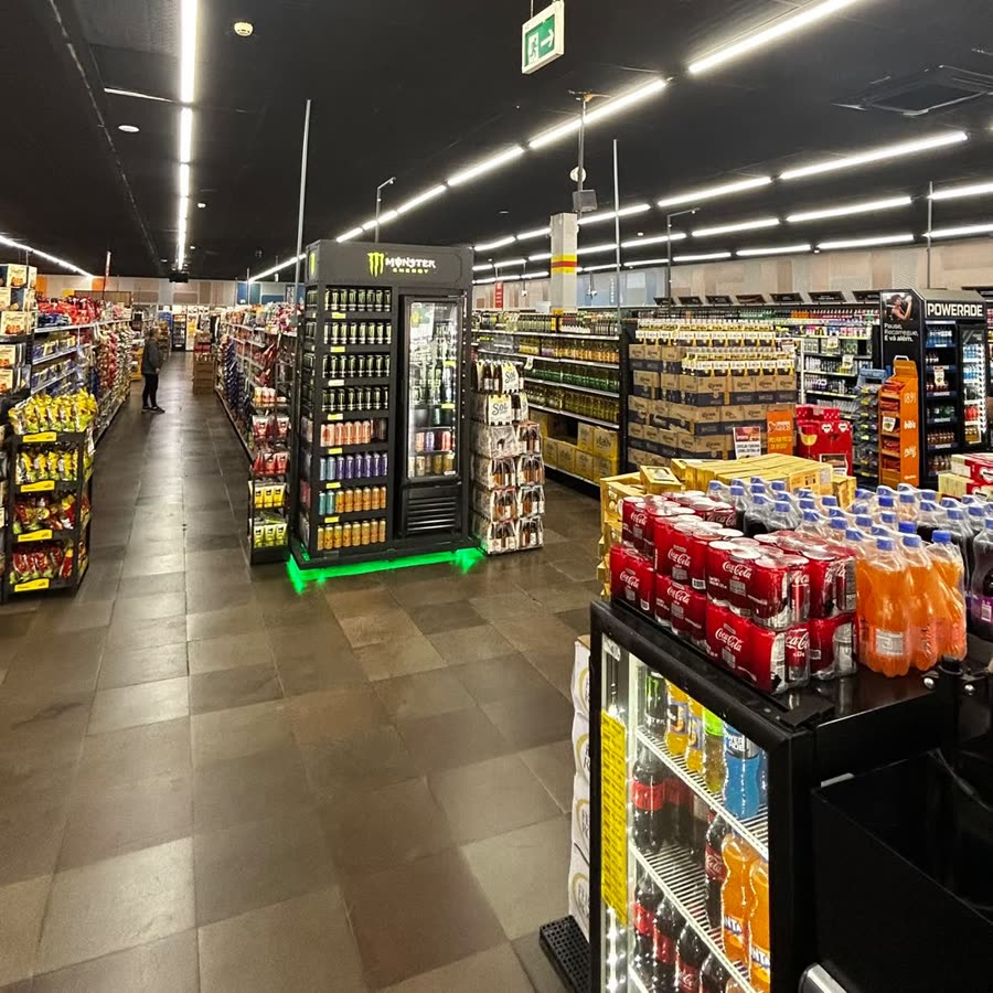 Corredor central da loja, com gôndolas dos dois lados e a geladeira de energéticos ao fundo